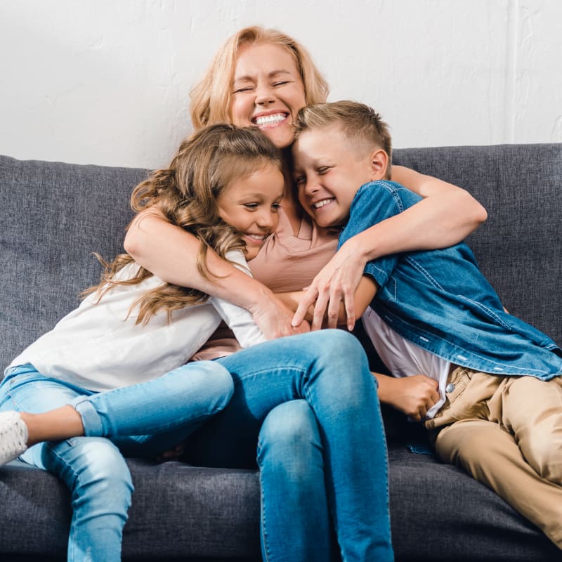 A woman is sitting on the floor with a young boy sitting in her lap facing her and laughing.