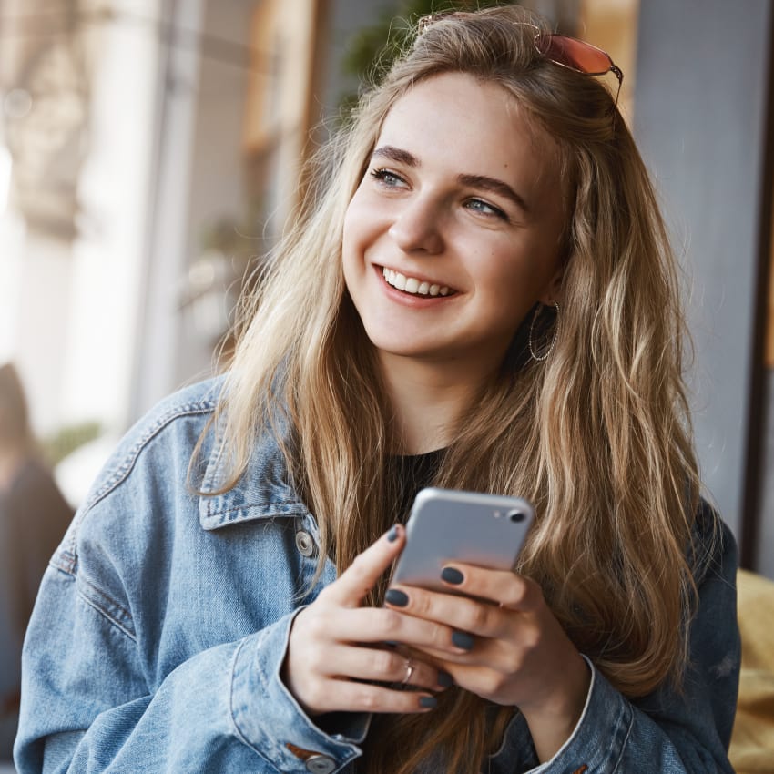 A woman with bright white teeth smiles at a man while she holds a take-out coffee cup.